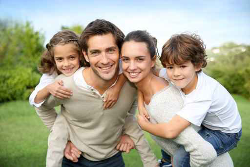 Das Bild zeigt eine Familie mit Mann, Frau und zwei Kindern. Der Vater hat die Tochter Huckepack und die Mutter trägt den Sohn auf den Schultern. Alle klächeln in Richtung Betrachter. Im Hintergrund sind eine Wiese und Büsche zu sehen.